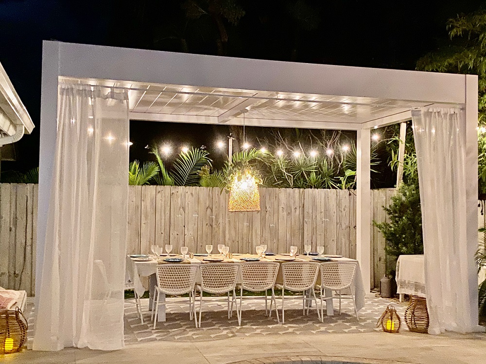 A white pergola with a chandelier and sheer white curtains