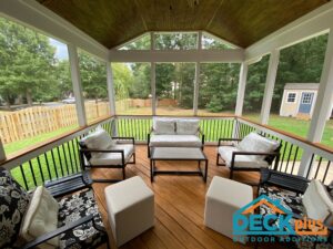 Custom screened porch with barrell ceiling and patio furniture. View of large yard and trees outside.