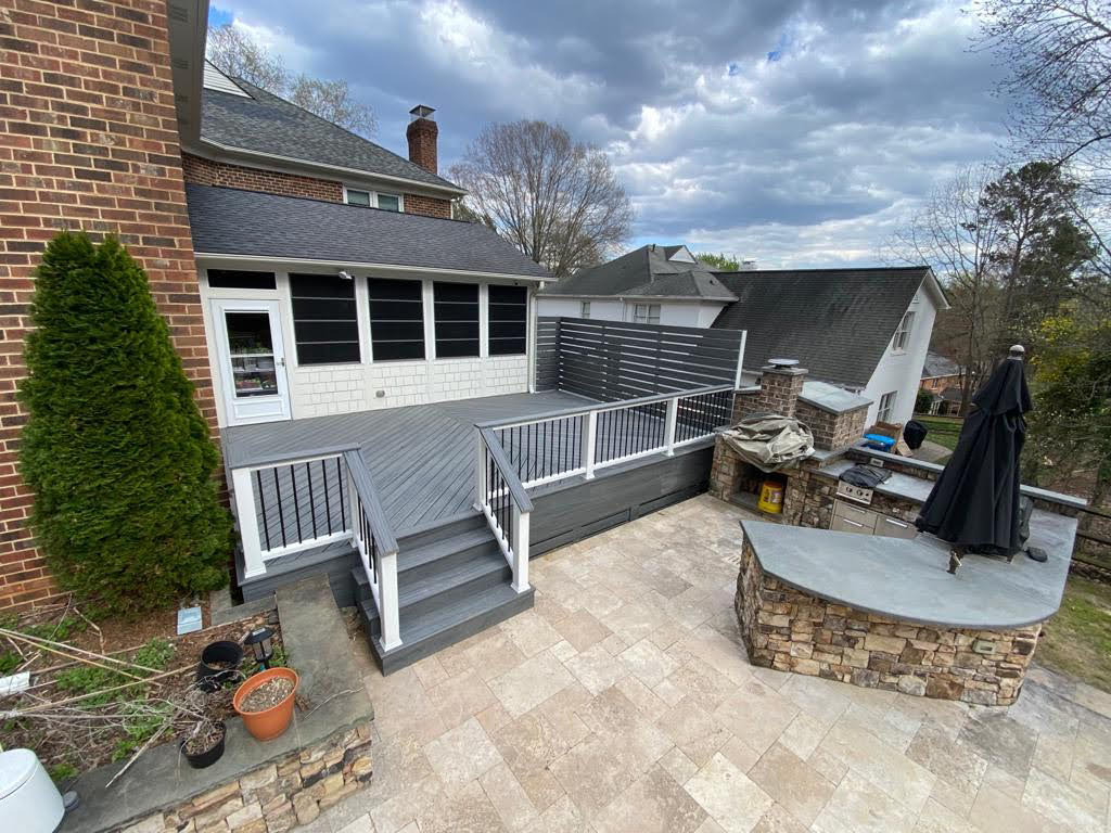 A painted wooden deck that leads onto a stone patio with an outdoor kitchen