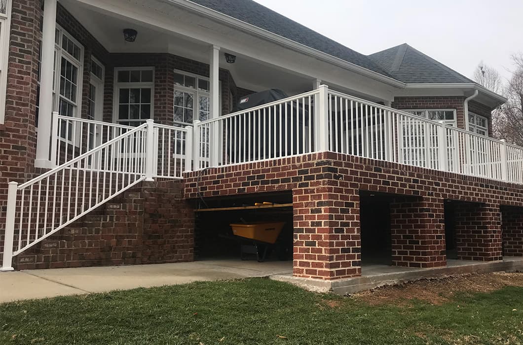 a brick house with a deck, white railings, and stairs