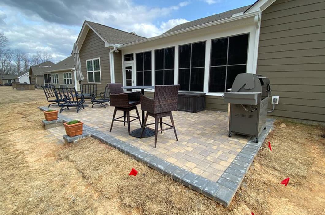 a brick patio with chairs and a grill in the middle