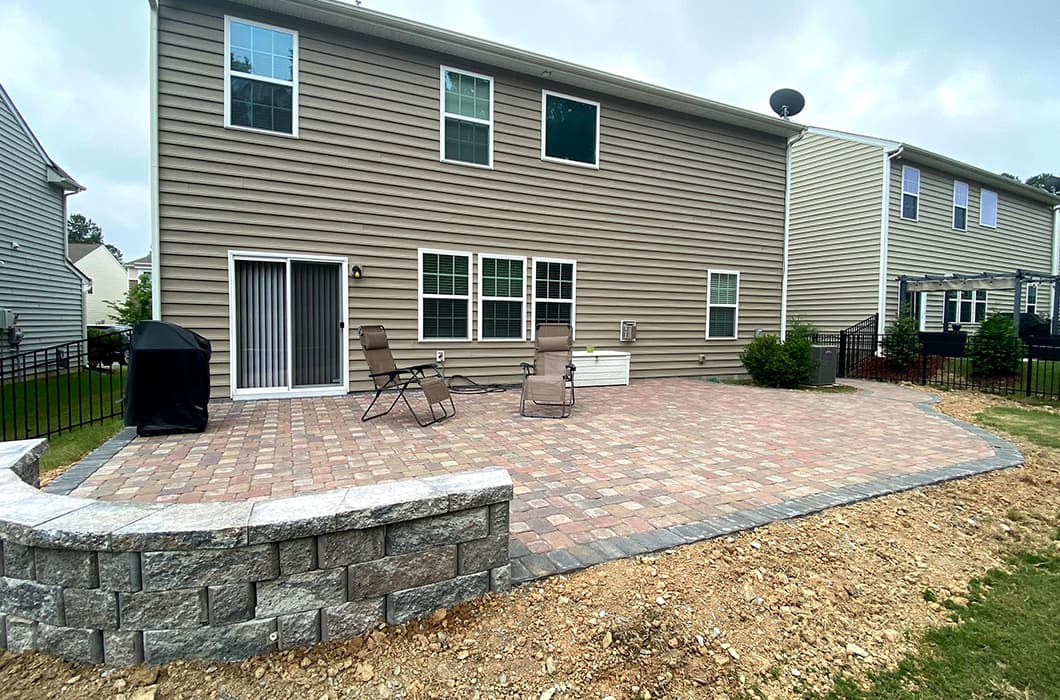 a brick patio in the backyard with loungers and a grill