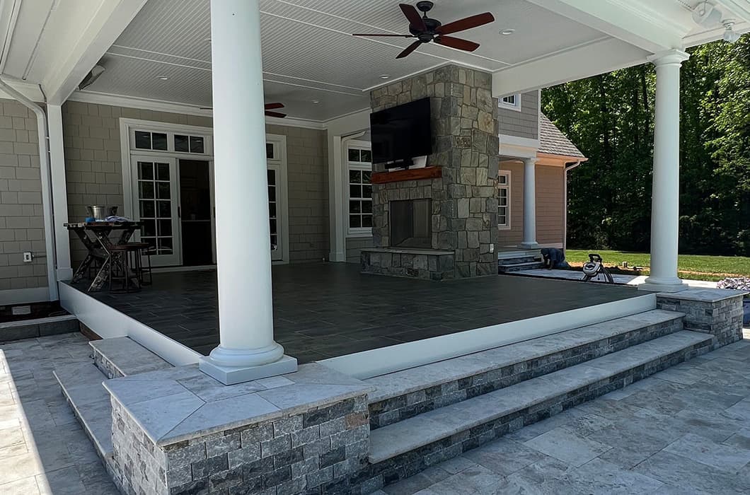 a covered stone patio with a fireplace and ceiling fan