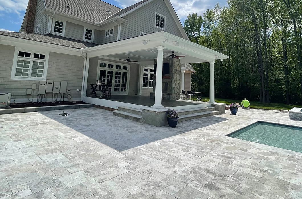 a covered back patio with a fireplace that leads onto a stone pool deck